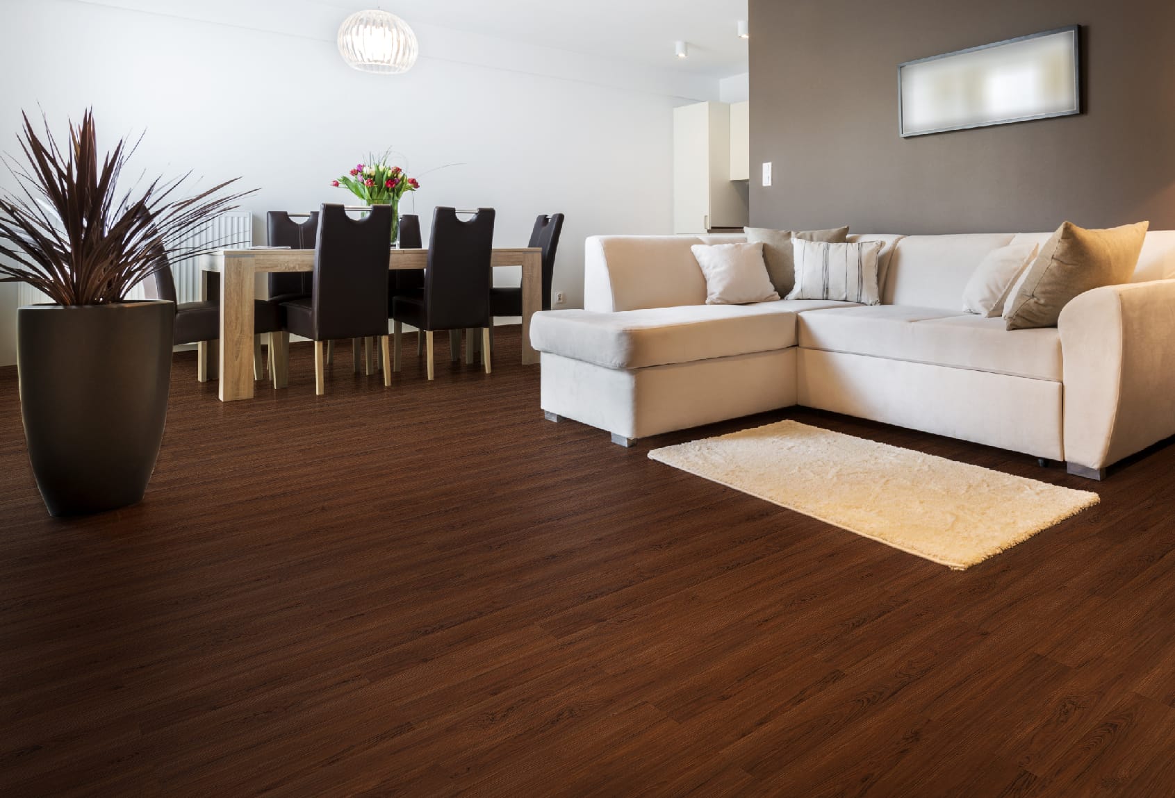 Lantai Vinyl TV 2004 Dark Applewood di Ruang Tamu dan Makan Modern - Penerapan lantai vinyl dengan desain Dark Applewood yang gelap dan elegan di ruang tamu dan ruang makan, menampilkan sofa krem, meja makan kayu, dan elemen dekorasi minimalis, menciptakan suasana hangat dan kontemporer dalam hunian